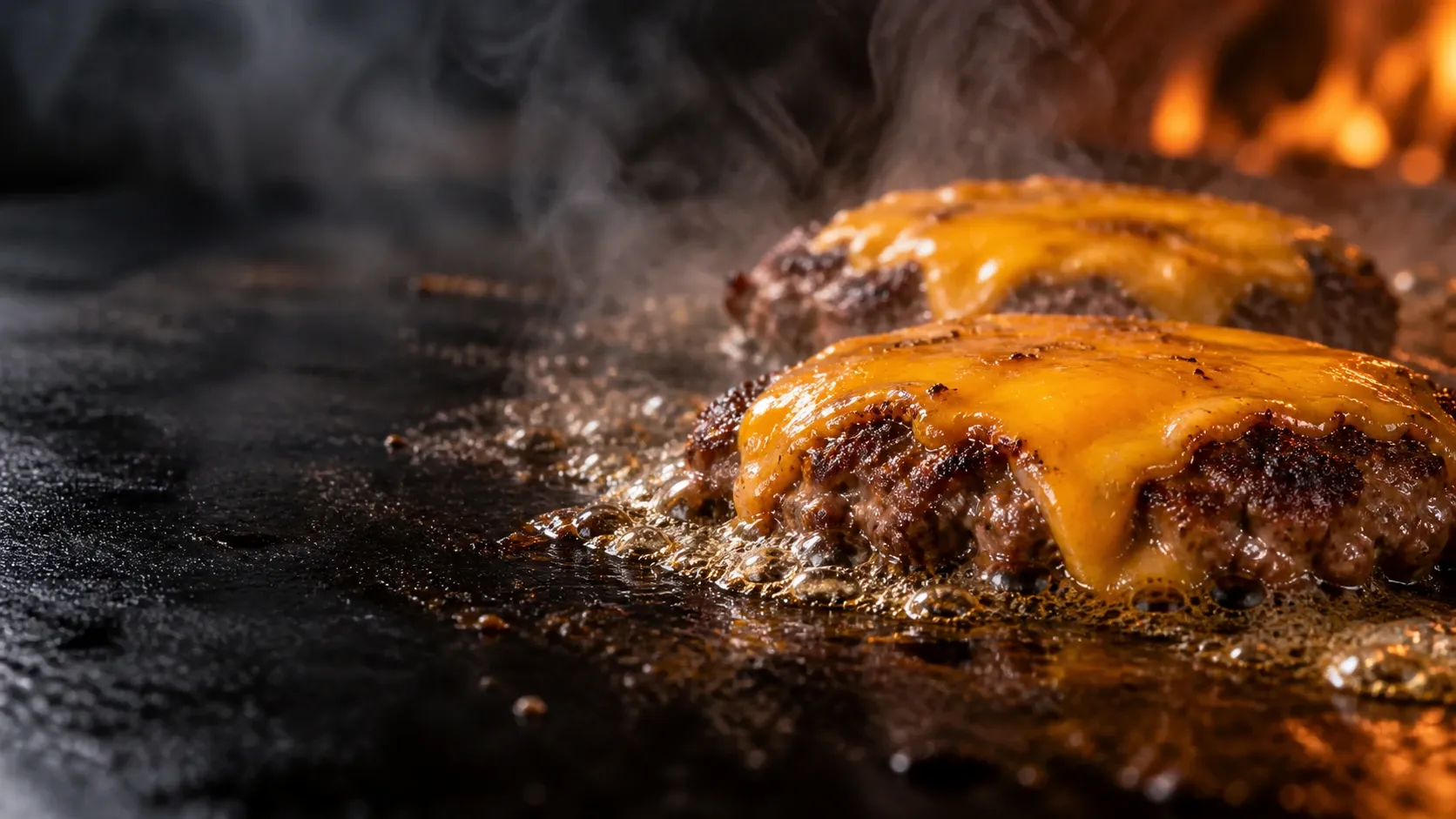 鉄板の上で肉汁が泡立ち、チェダーチーズがとろけるパティ